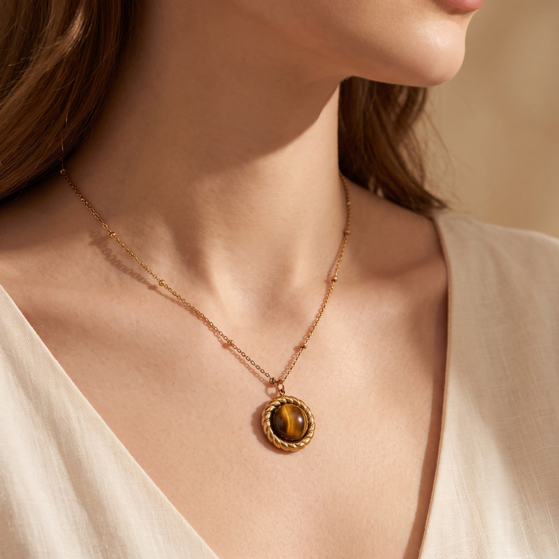 Side view of a model wearing a gold-tone station chain with a round brown cabochon pendant over a white top