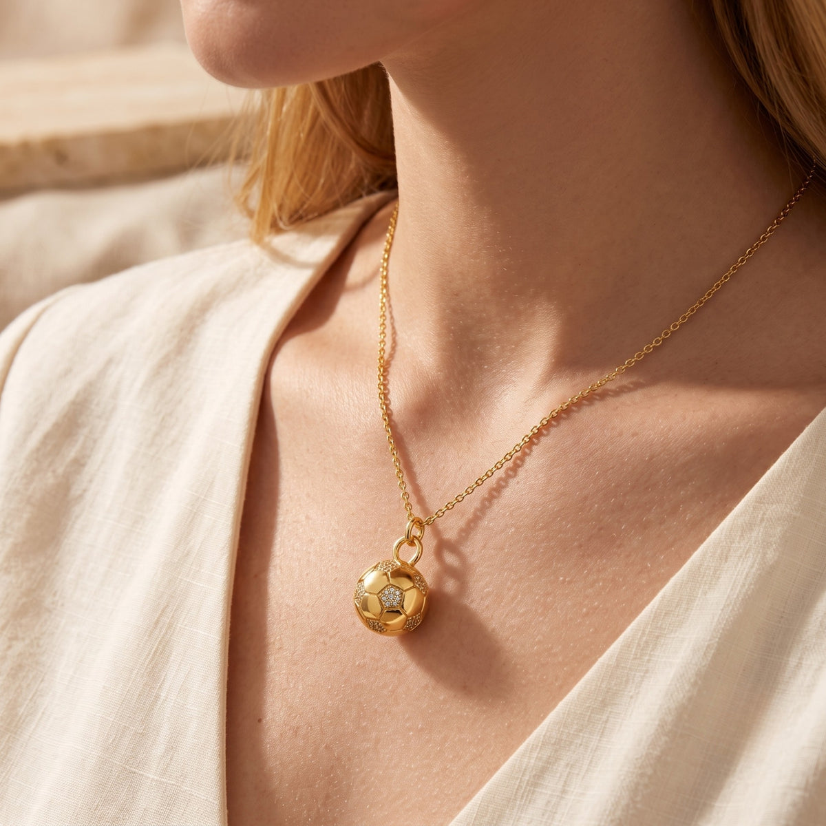 Model wearing the gold-tone soccer ball pendant necklace, angled close-up view against a v-neck top.