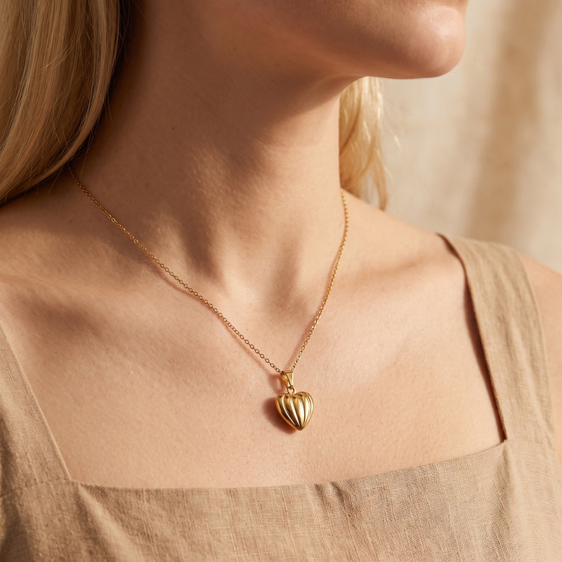 Side view of a woman wearing the gold-tone ribbed heart pendant necklace with a square-neck beige top.