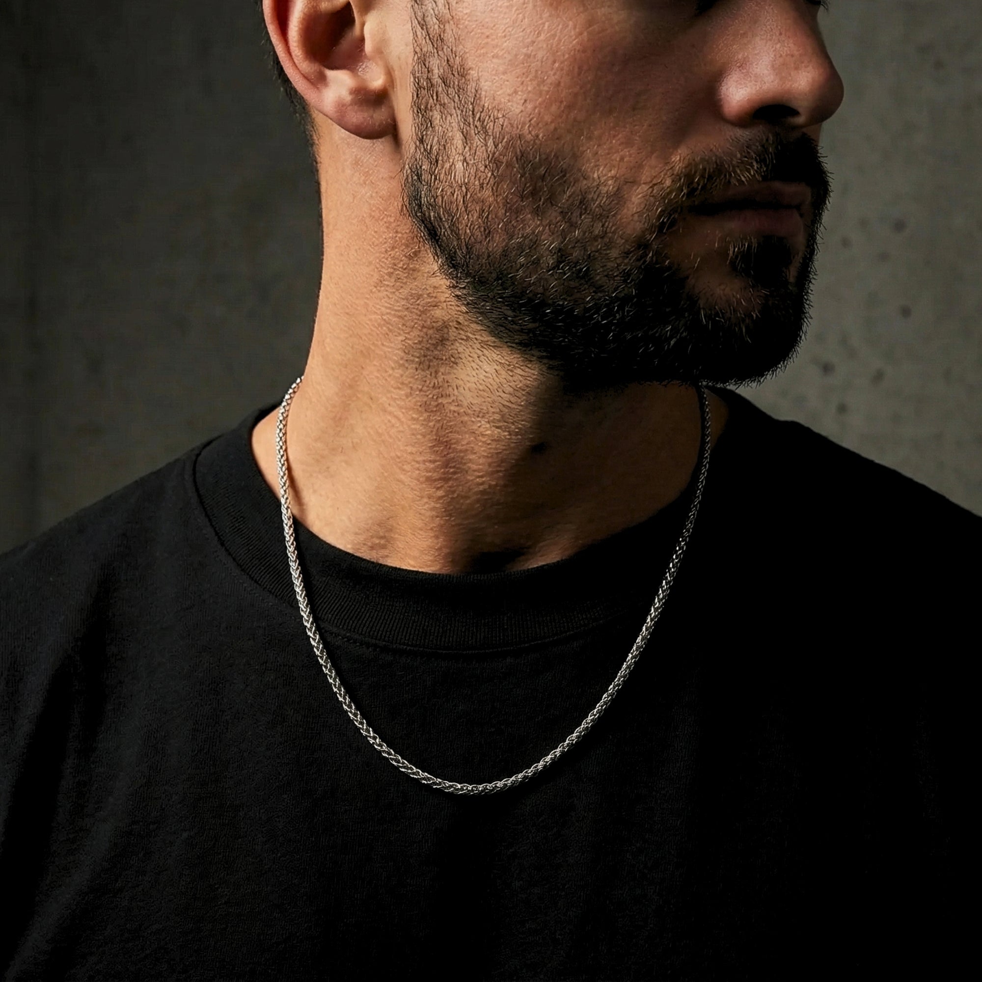 Men's silver stainless steel wheat weave chain necklace worn by a model in a black t-shirt.