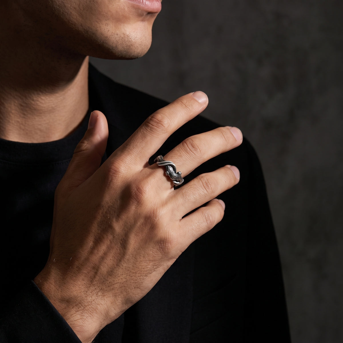 Model wearing the textured silver open band ring on his middle finger against black clothing.