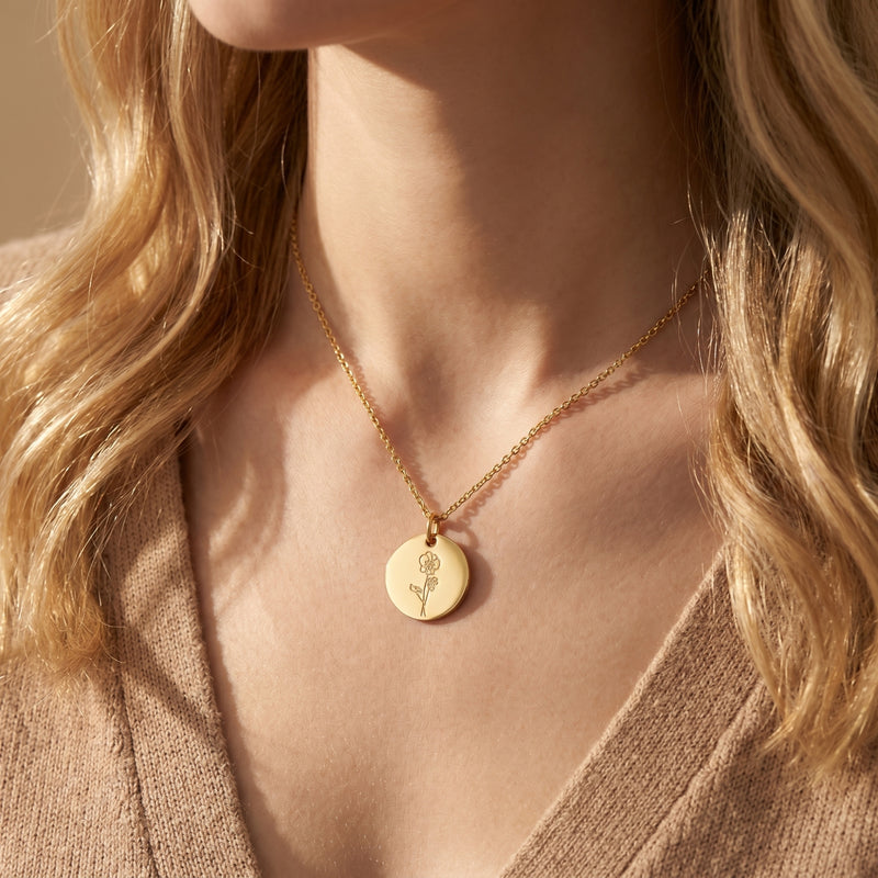 Woman wearing the 18K gold finish Botanique birth flower necklace with an engraved circular pendant.