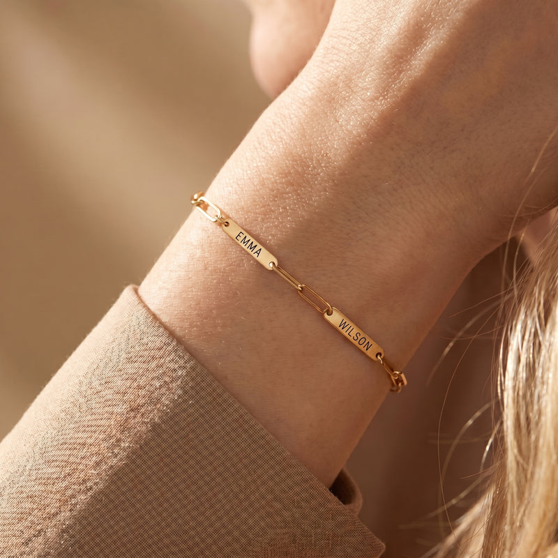 Gold personalized link bracelet with engraved name plates EMMA and WILSON worn on a wrist.