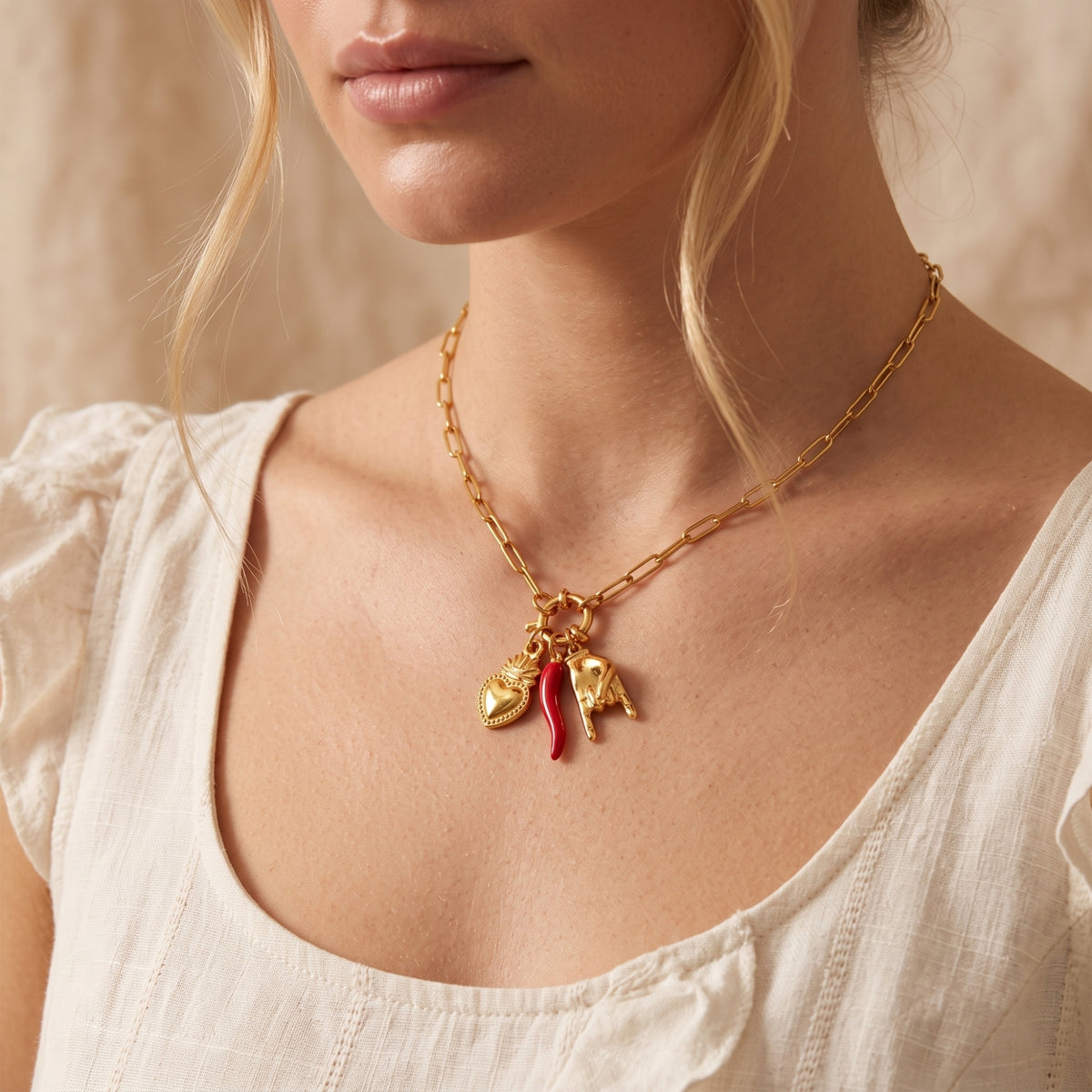 Woman wearing the gold-tone paperclip necklace with three charms against a white ruffled top.