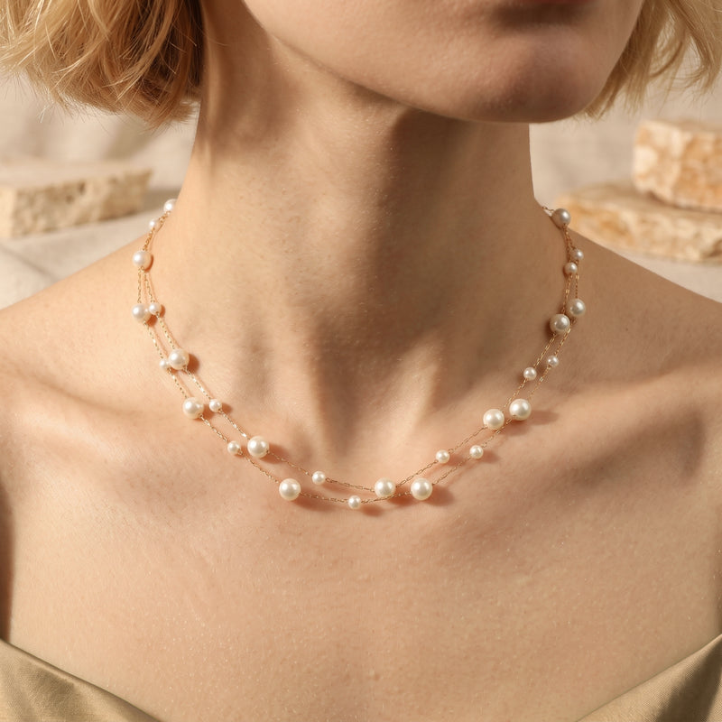 Model wearing the double-strand gold-tone station necklace with white pearls along the neckline.