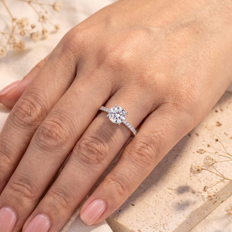 Top view of the silver ring with a round clear center stone worn on a hand against a light neutral background.