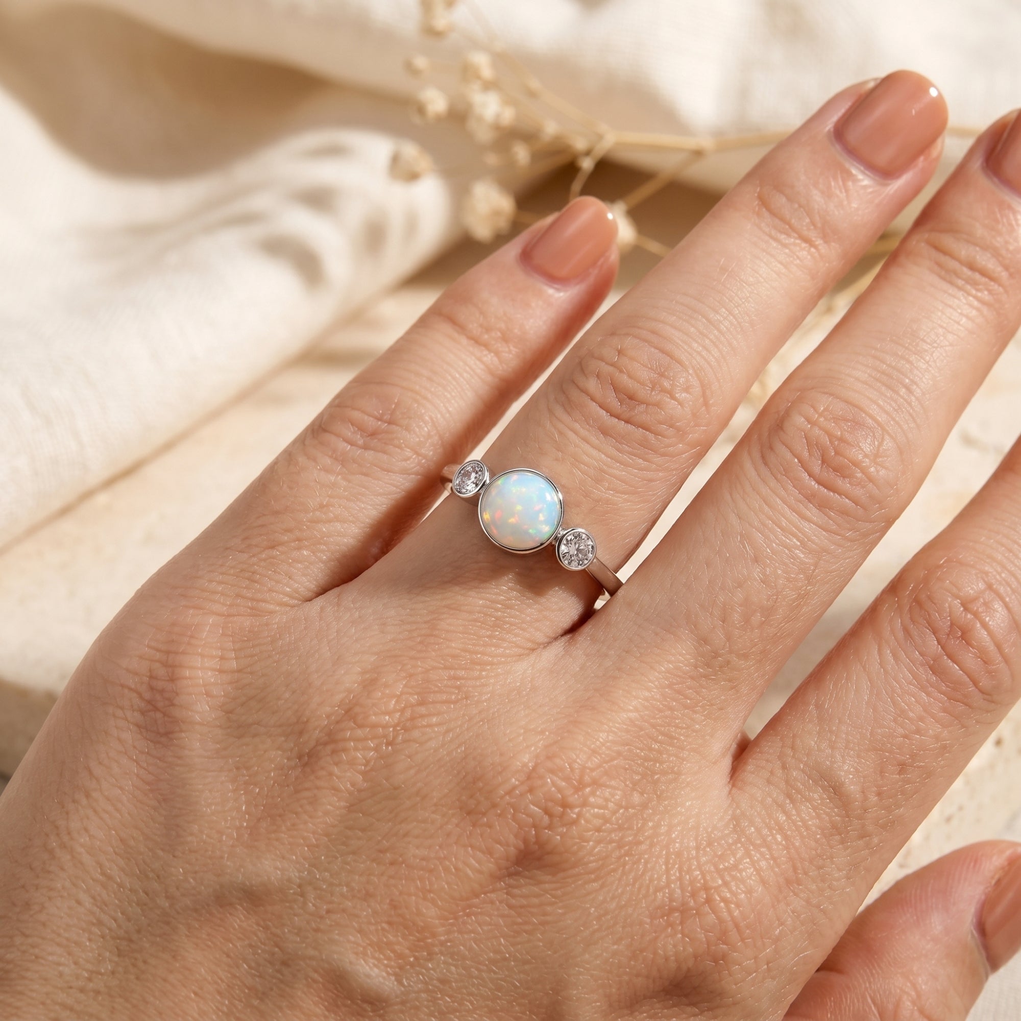 Top view of a round white opal and zircon sterling silver ring worn on a woman's hand.