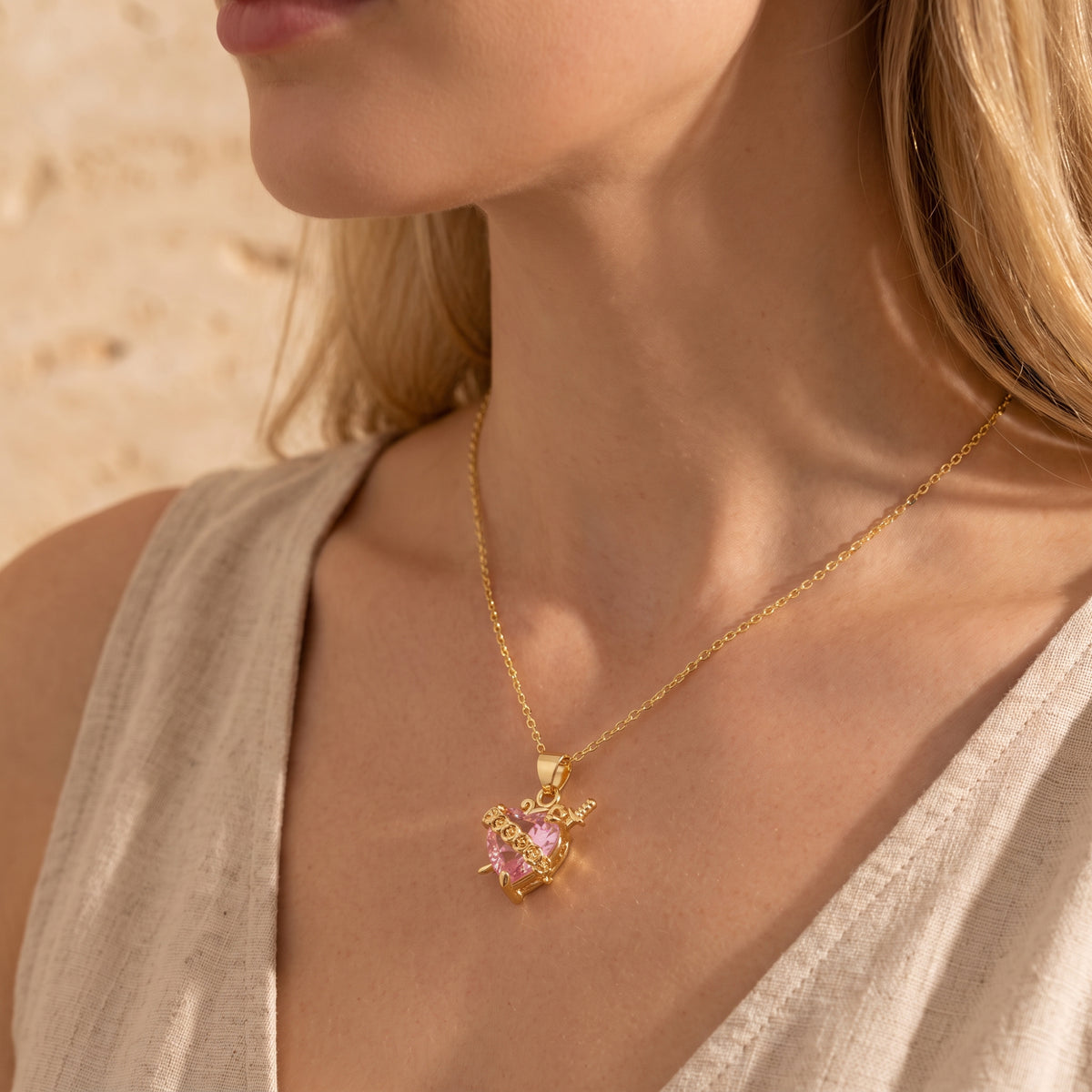 Side angle of a model wearing the gold-tone necklace with a pink heart crystal pendant.