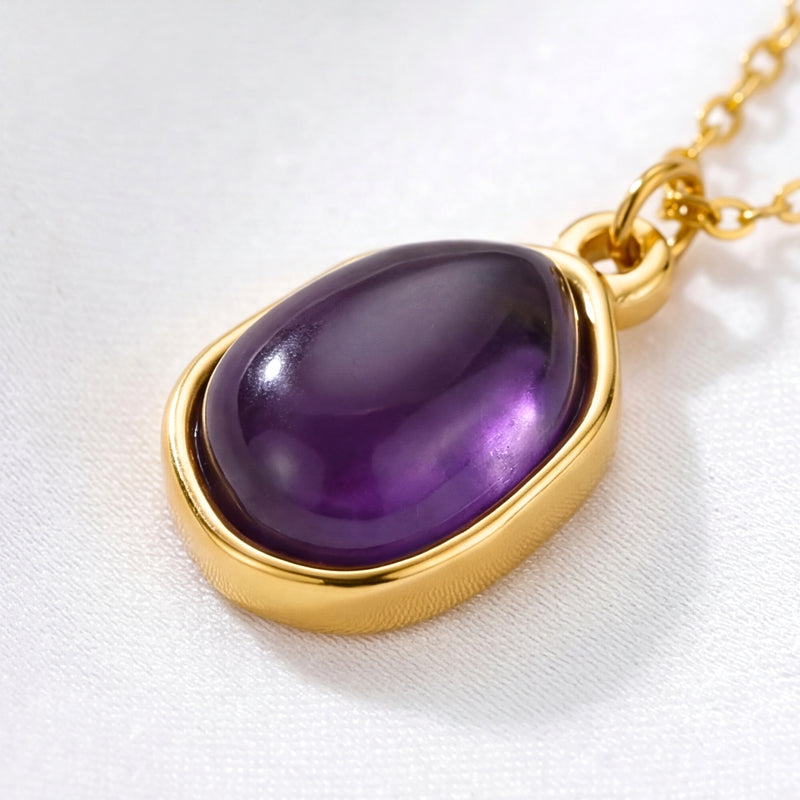 Macro view of a purple teardrop simulated amethyst pendant in a polished yellow gold setting.