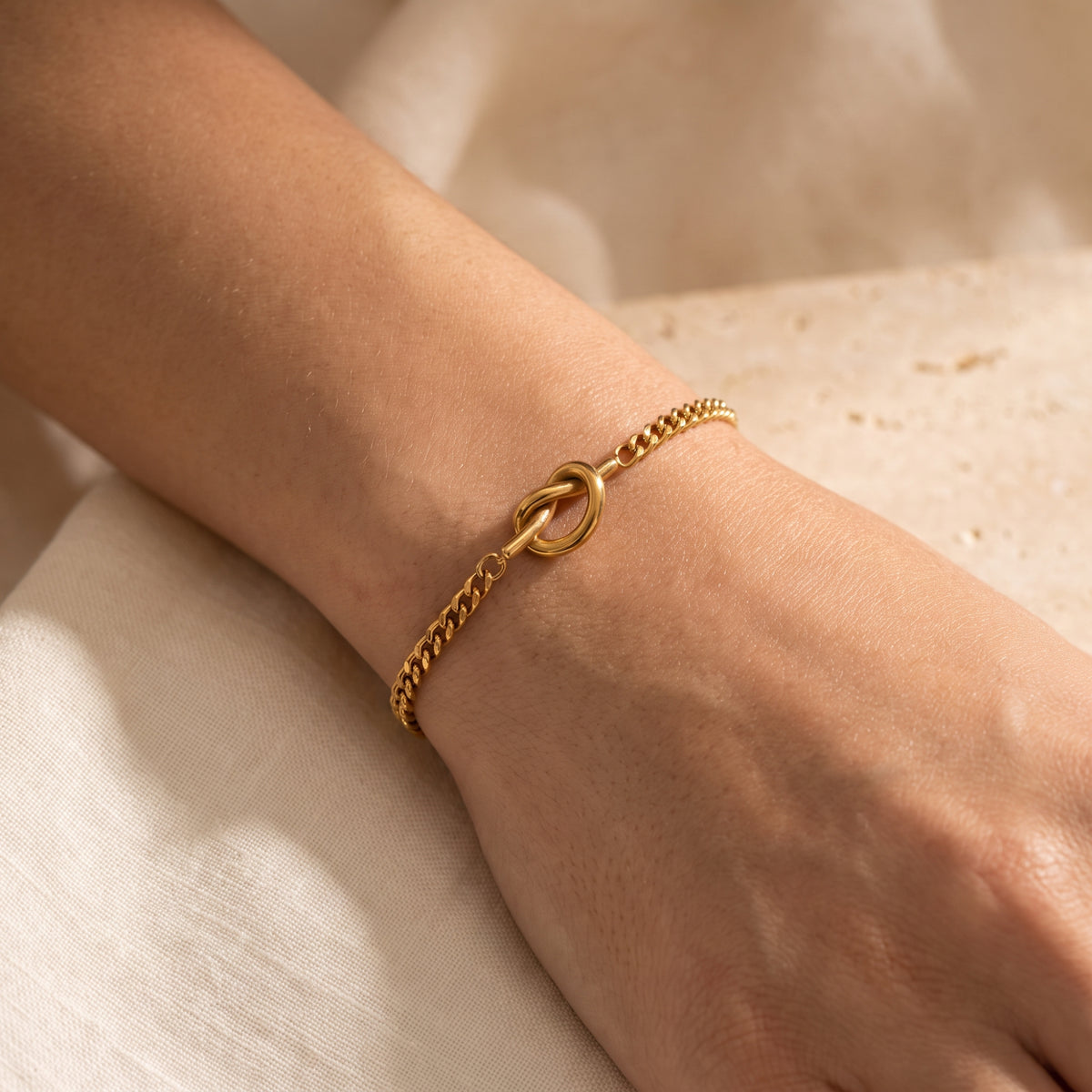 Close-up of the gold-tone knot link bracelet worn around a wrist, with the knot feature centered.