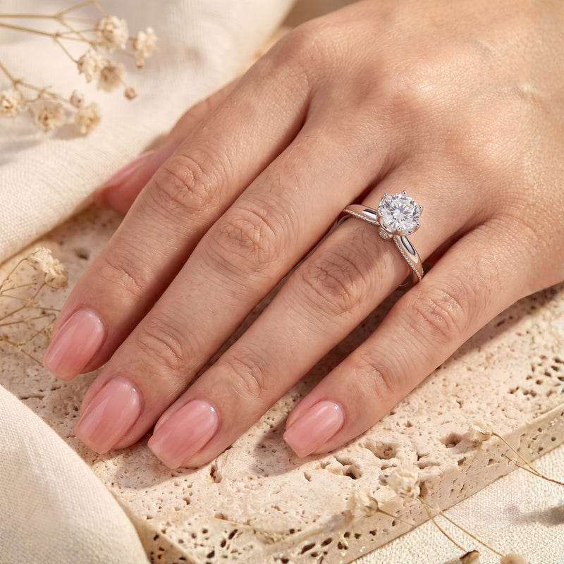 Model wearing the silver round-cut solitaire ring on her ring finger against a warm textured backdrop.