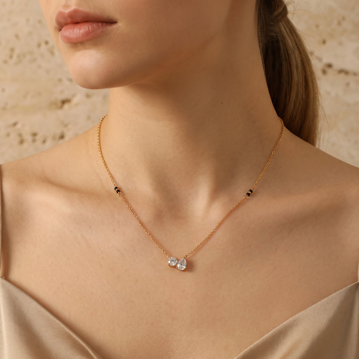 Model wearing the gold-tone necklace with round and pear-cut clear stones and black bead details along the chain.