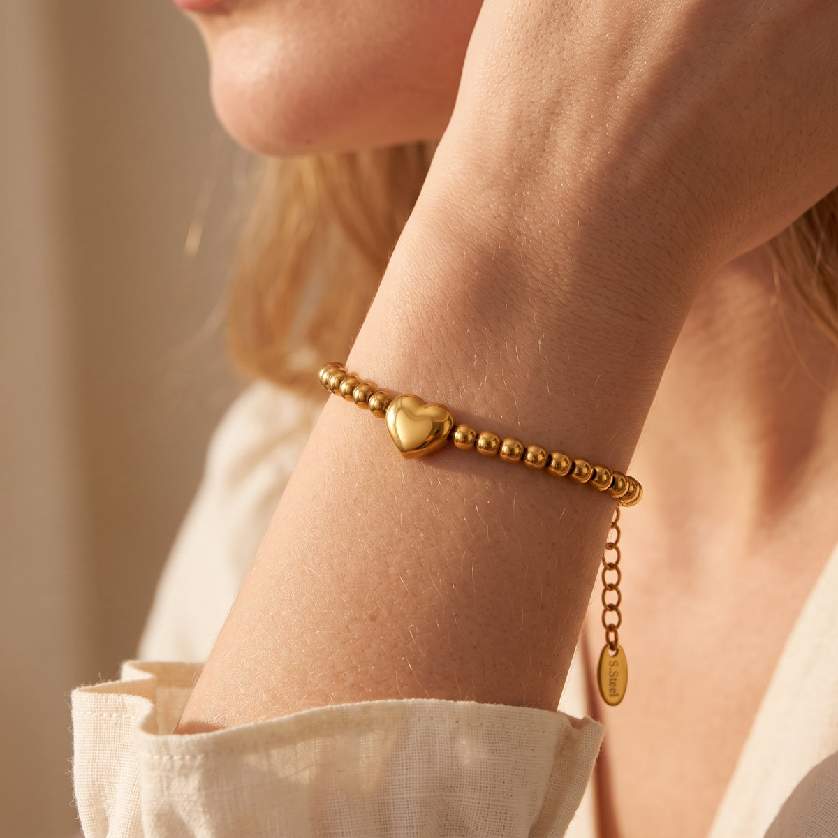 Close-up of the gold-tone beaded heart bracelet worn on a wrist, featuring a dangling extender chain.