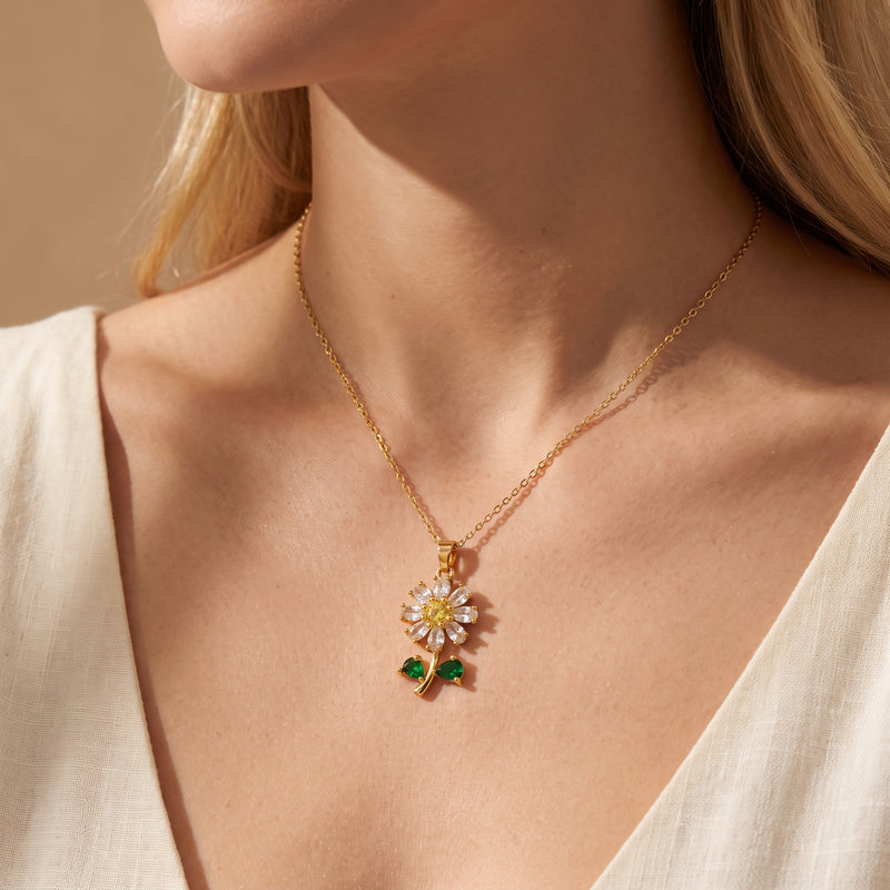 Close-up of a model wearing the gold-tone daisy pendant necklace with a yellow center stone and green leaf accents.