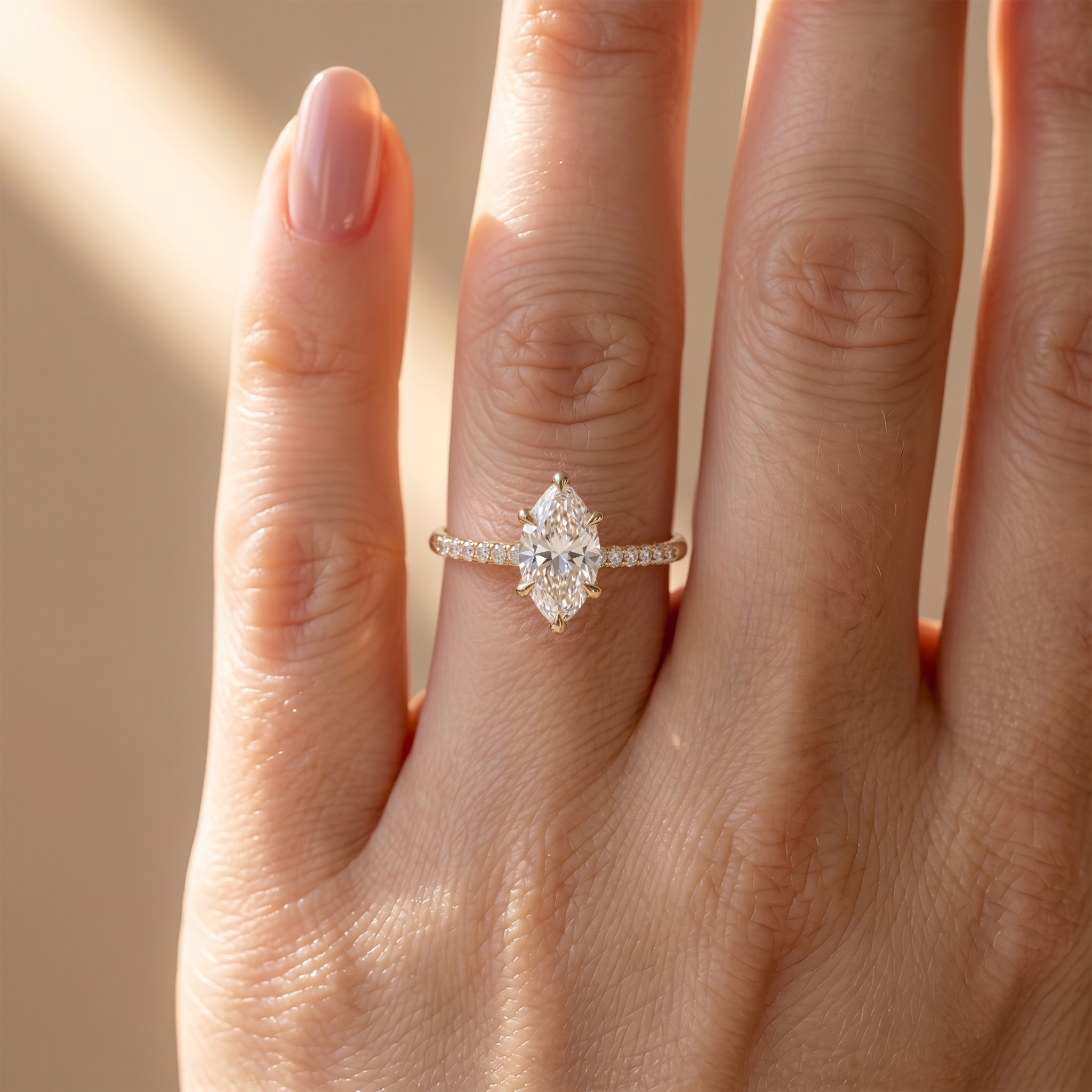 A close-up view of a yellow gold marquise-cut moissanite engagement ring with a pavé diamond band worn on a model's finger.