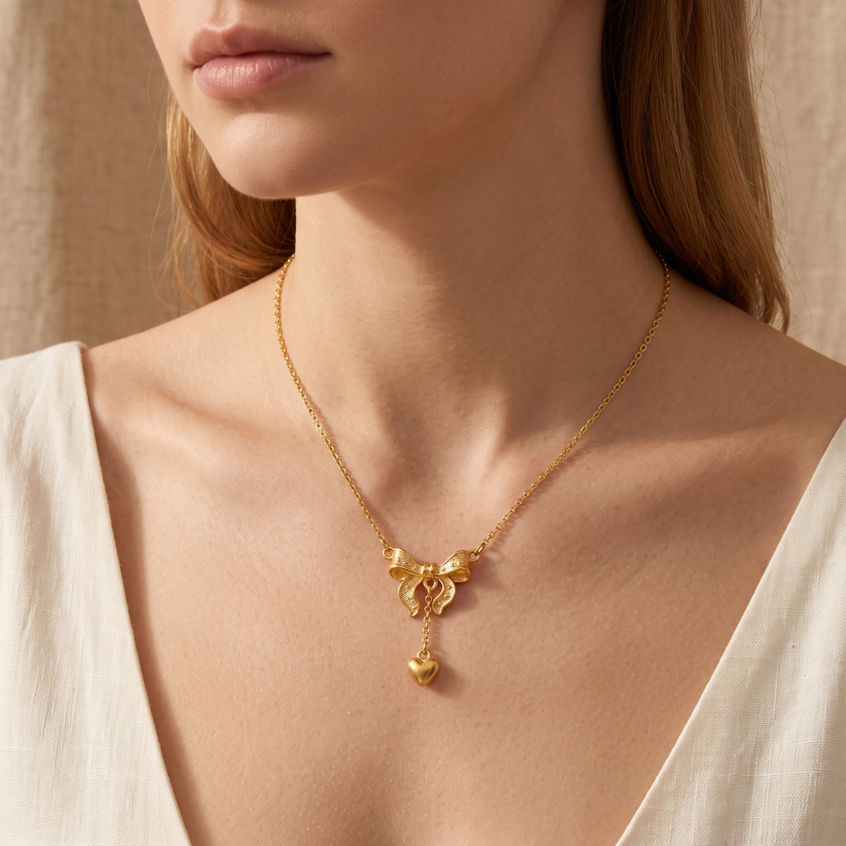 Model wearing the gold-tone bow and heart pendant necklace, shown in a close-up against a white top.