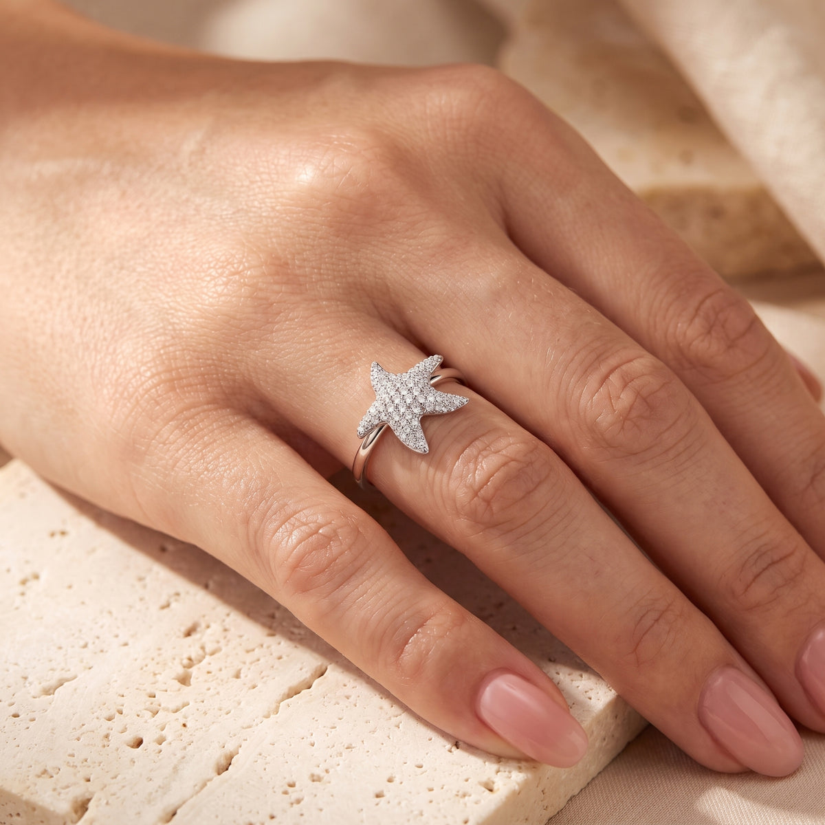 Top-down view of a hand wearing a silver starfish ring with pave-set clear stones.