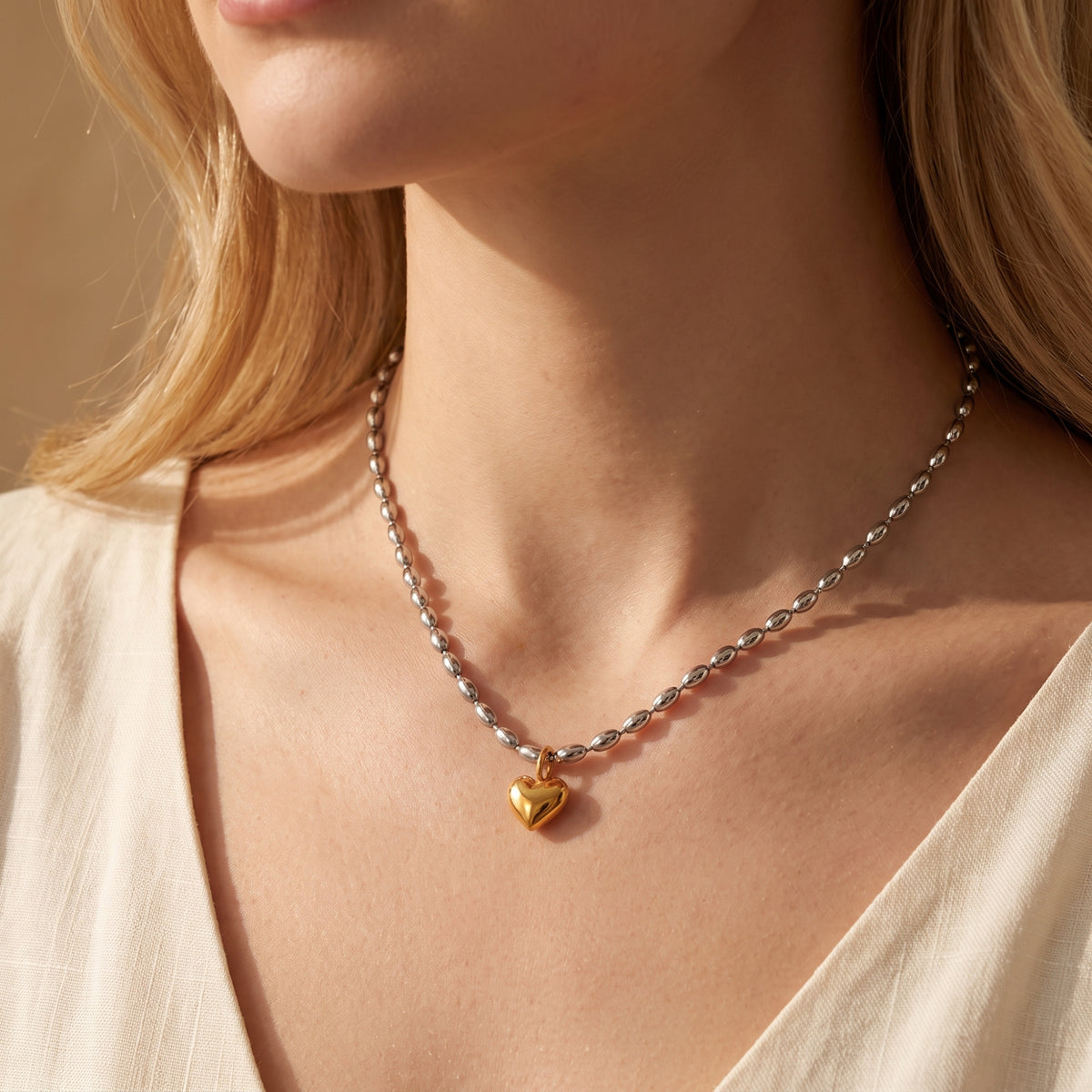 Close-up of a model wearing the two-tone necklace with a silver bead chain and gold heart pendant.