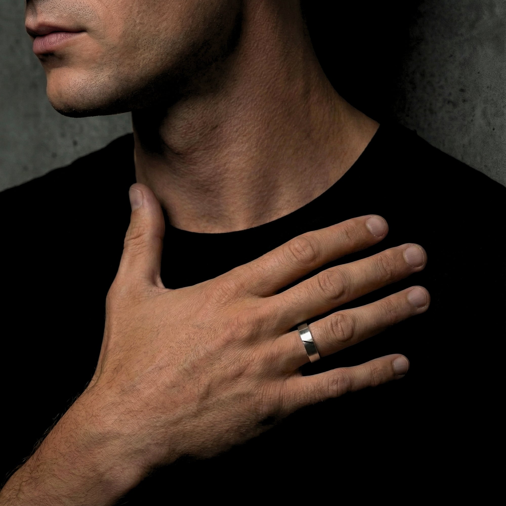 Men's brushed silver stainless steel Spartan band ring worn on a model's ring finger against a black shirt.