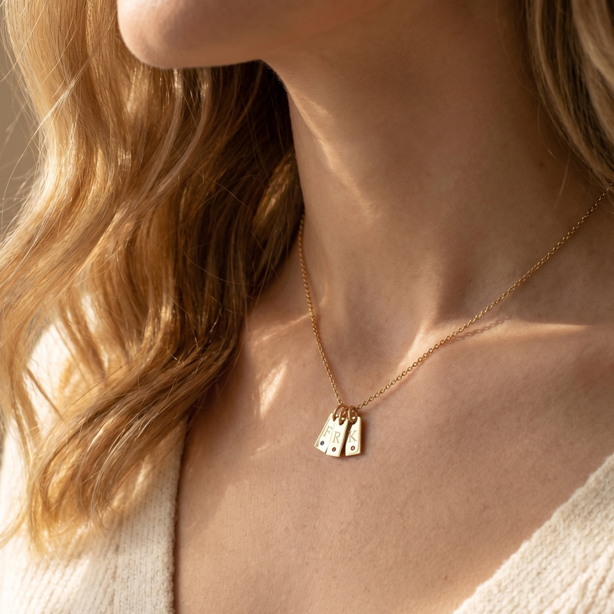 Woman wearing the gold Cecelia pendant necklace with three personalized initial tags and small round birthstones.