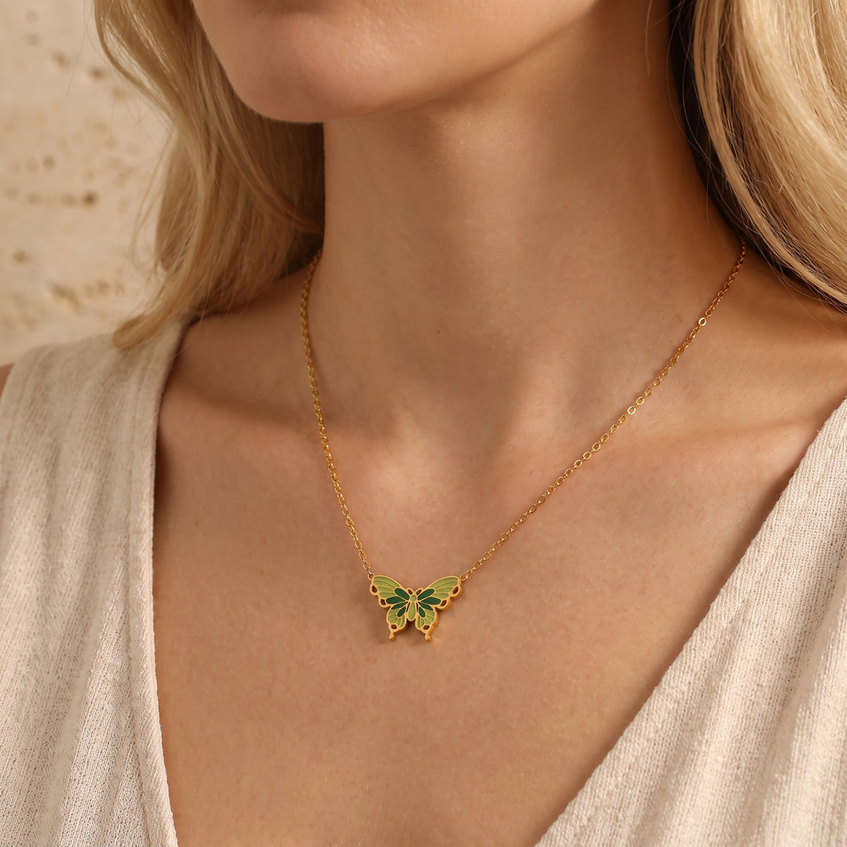 Gold-tone butterfly necklace with green and olive enamel wings shown on a model’s upper chest.