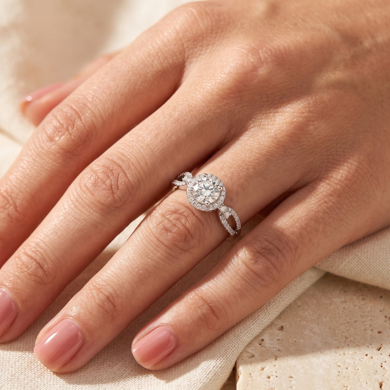 Angled view of the halo ring with a round center stone and pavé infinity twist band worn on a finger.