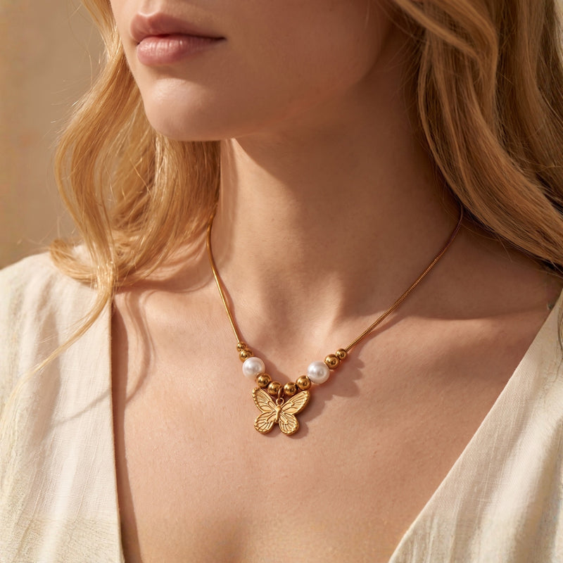 Model wearing a gold-tone butterfly pendant necklace with two white pearls and gold beads.