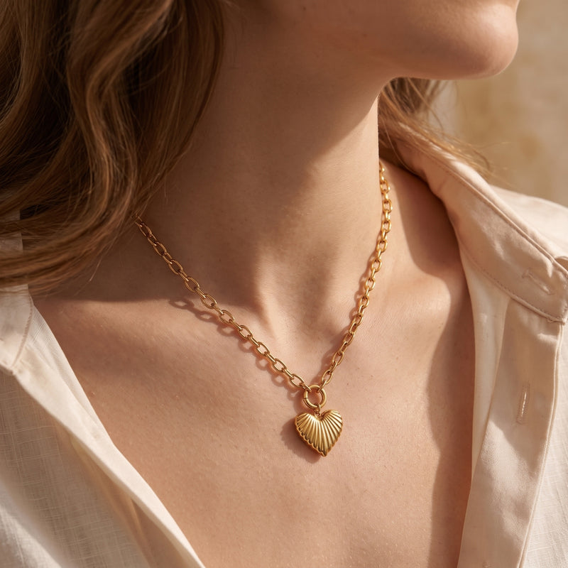 Model wearing the gold-tone ribbed heart pendant necklace with a cream open-collar shirt.