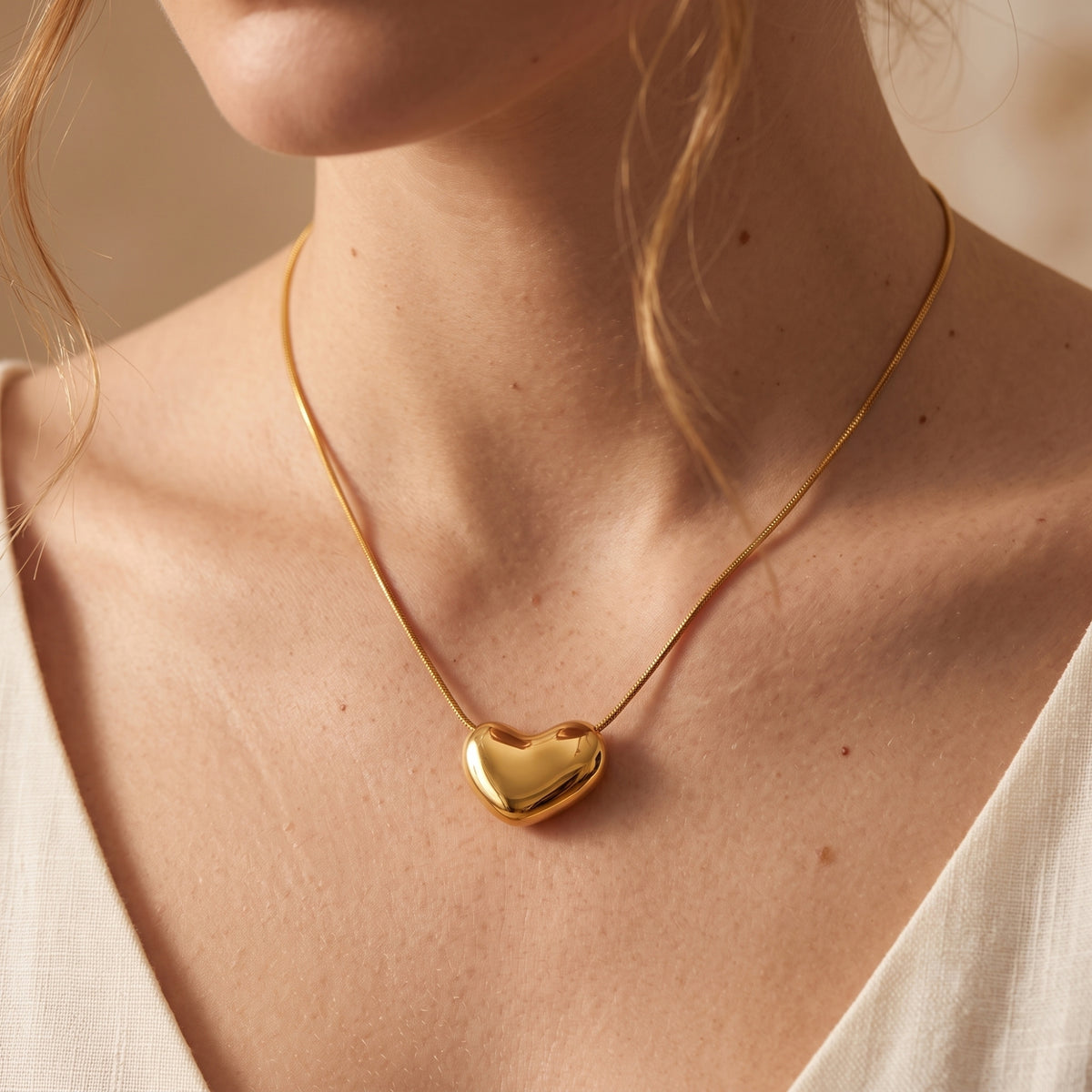 Front view of a model wearing a gold-tone puffy heart pendant necklace near her collarbone.