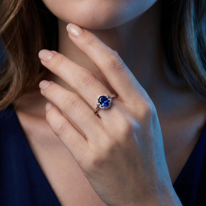 Woman wearing the 18K white gold oval tanzanite and diamond halo ring on her finger.