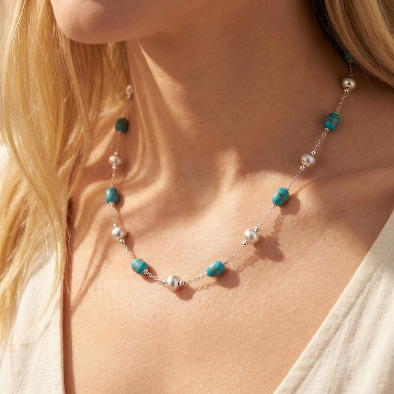Model wearing the Pueblo turquoise and silver bead necklace with a white linen top.