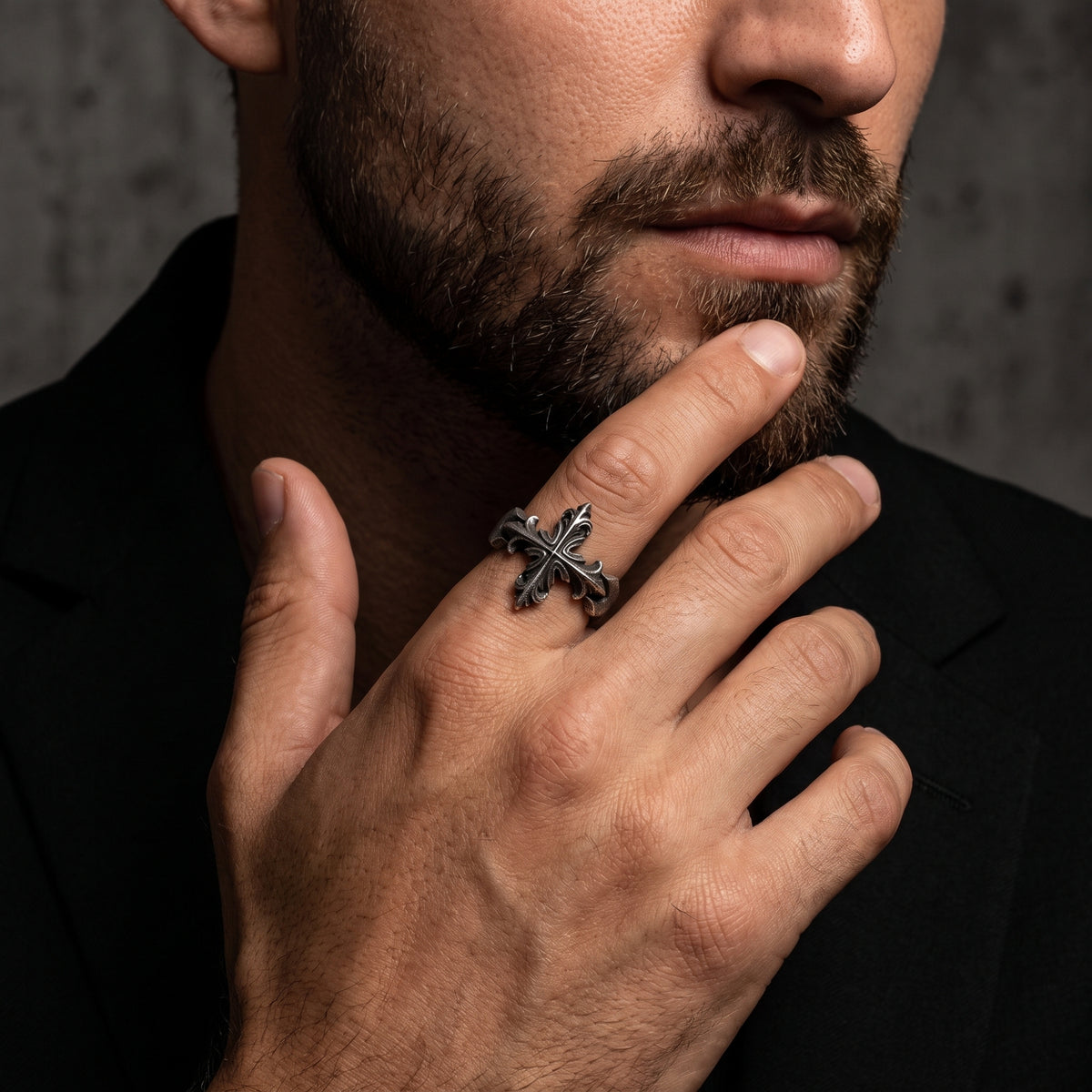 Close portrait of a man wearing the silver Gothic cross ring on his middle finger near his chin.