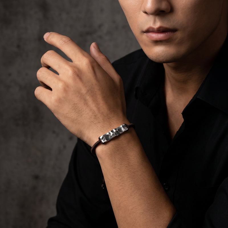 On-model shot of a man wearing the silver hammered bar bracelet on his wrist with a black shirt.