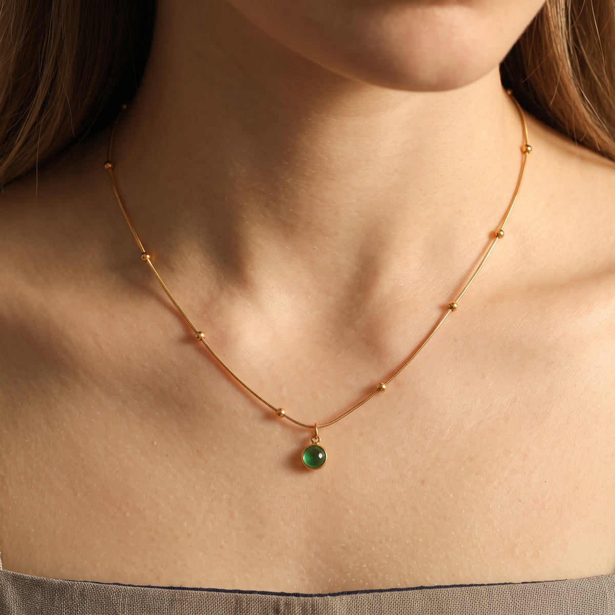 Model wearing a gold-tone station-bead necklace with a small round green agate pendant at the collarbone.