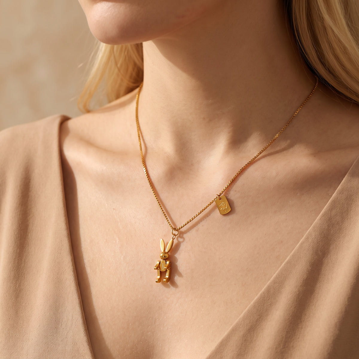 Model wearing the gold articulated rabbit necklace over a neutral beige V-neck top.