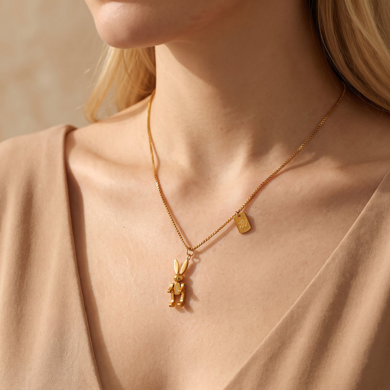 Model wearing the gold articulated rabbit necklace over a neutral beige V-neck top.