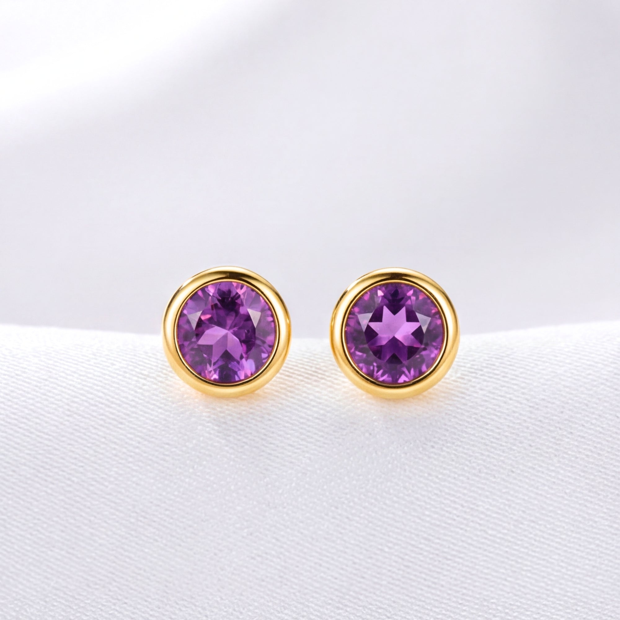 Macro shot of two round precision-cut simulated amethyst stones in 18K gold vermeil bezel settings.