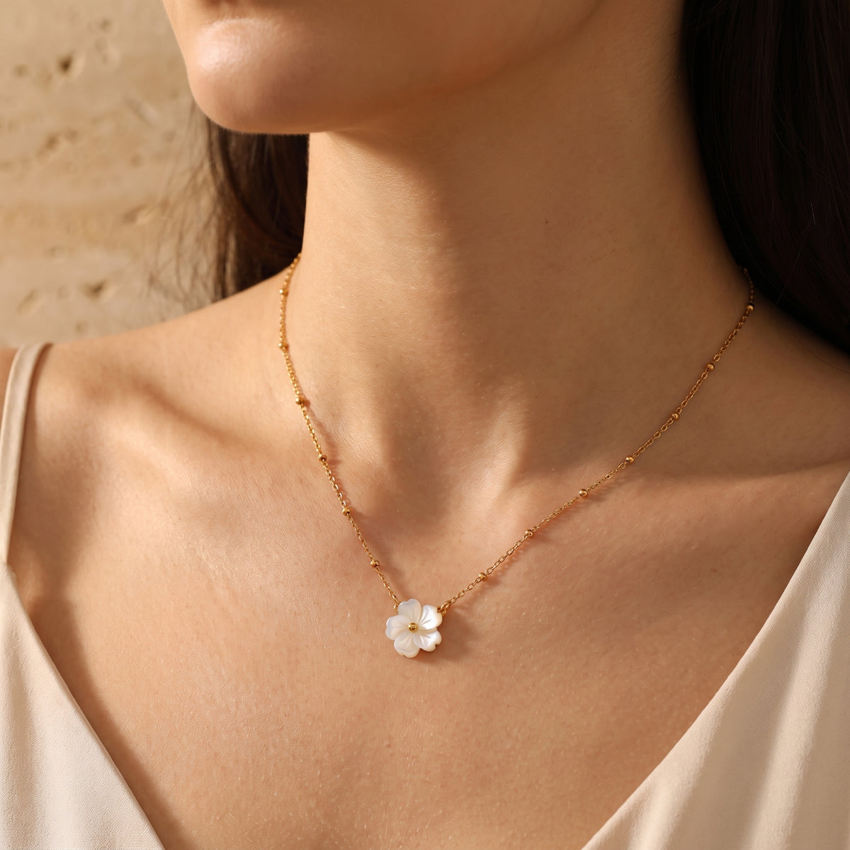 Front view of a gold-tone bead-station necklace with a carved white flower pendant worn on a model.