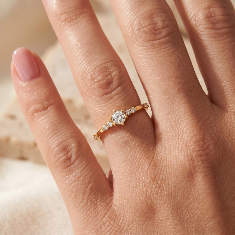Gold round cut moissanite ring worn on a model's finger with a pink manicure.