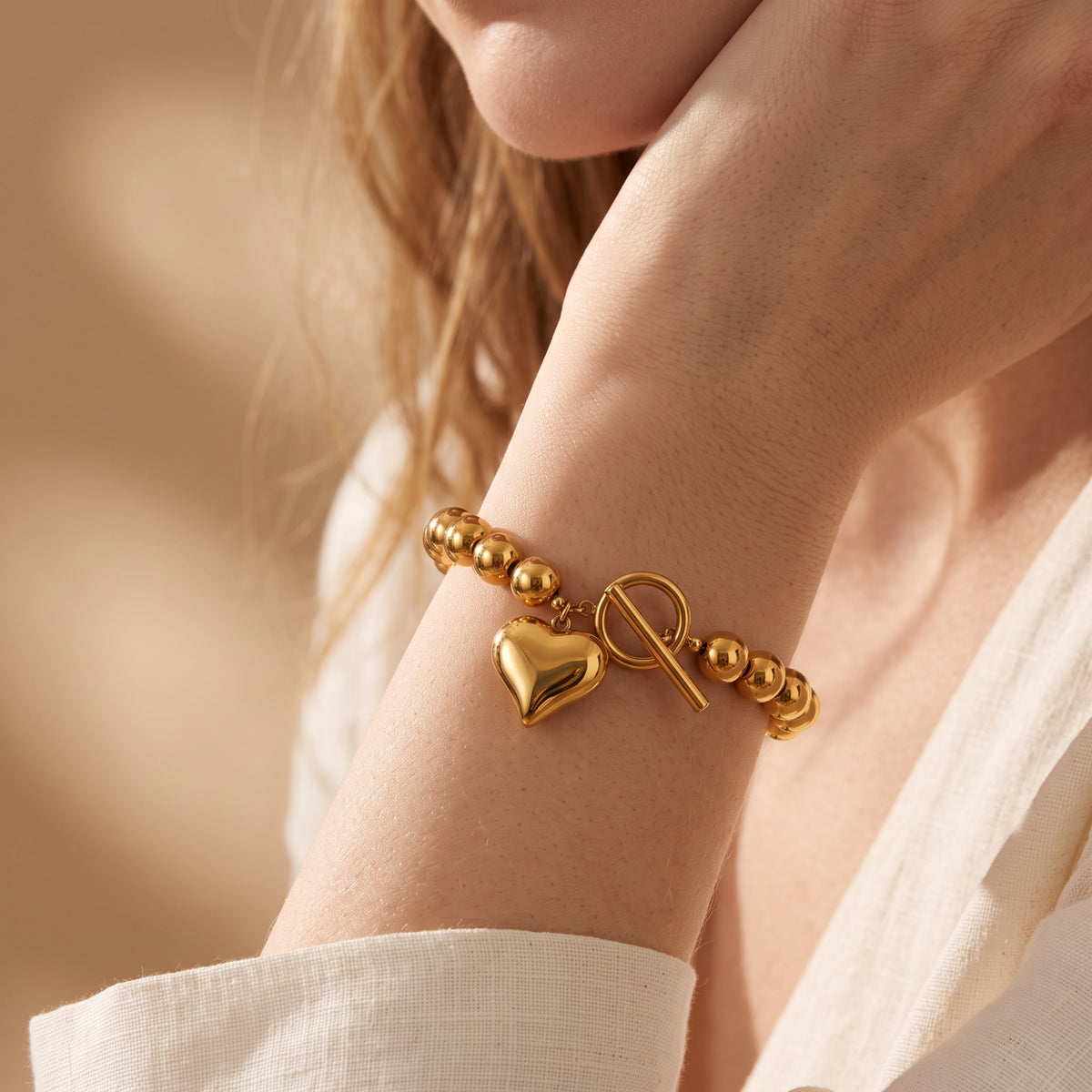 Close-up of a model wearing the gold-toned beaded bracelet with heart charm and toggle clasp on her wrist.