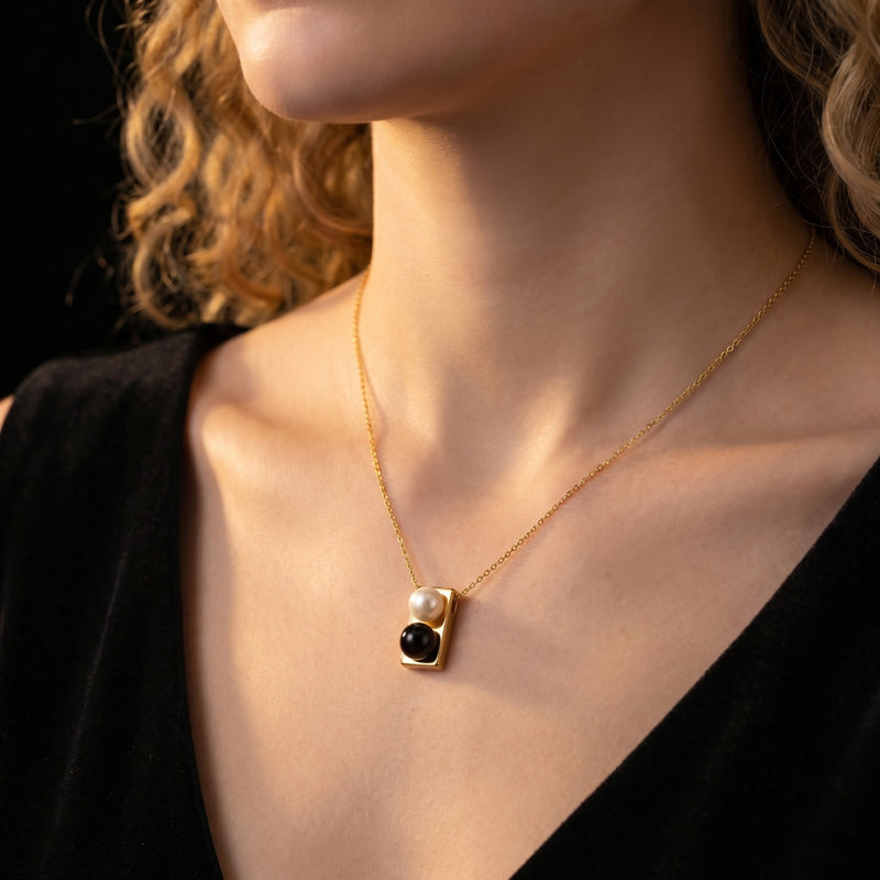 Gold Equilibrium Onyx Necklace with a white pearl and black onyx pendant worn on a model's neck.