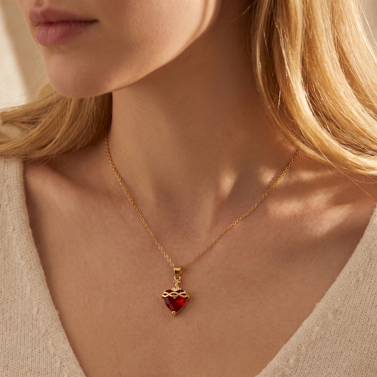 Sacred Heart necklace with a red heart crystal and gold-tone chain worn on a woman's collarbone.