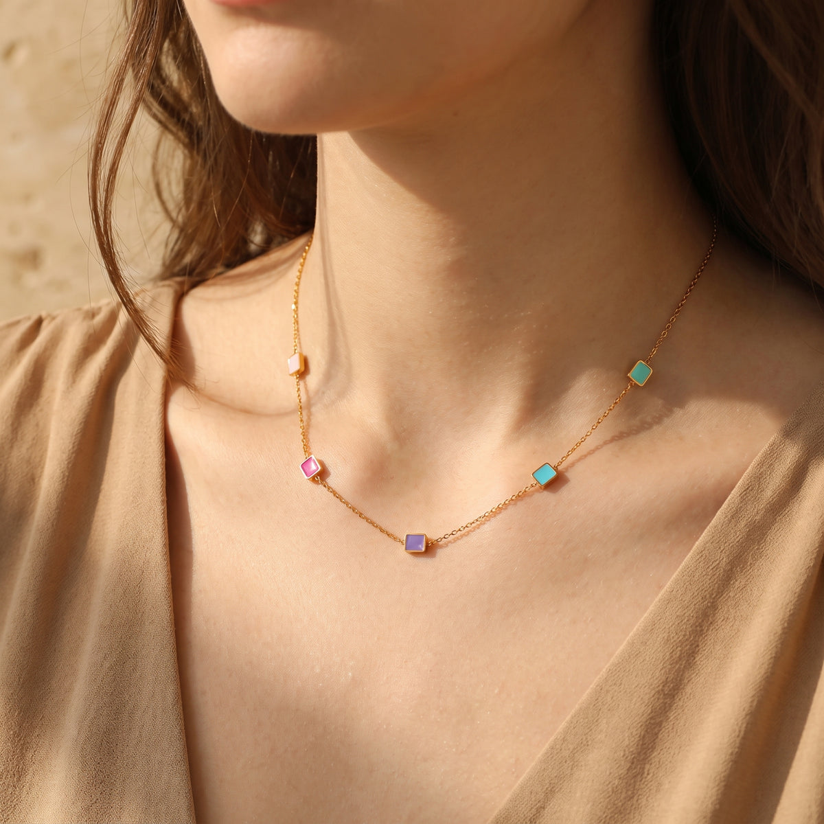 Model wearing a gold-tone chain necklace with multicolored enamel square stations and a tan top.