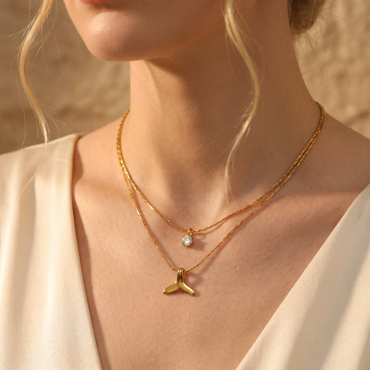 Model wearing the double-layered gold-tone necklace with a clear crystal solitaire and whale tail pendant.