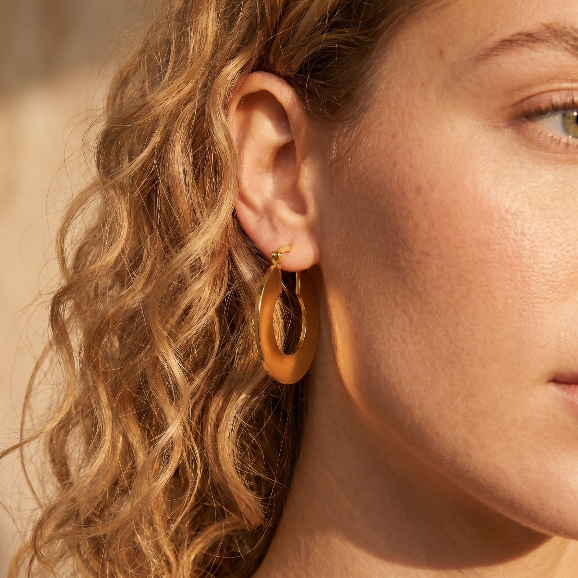 Side view of a model wearing a matte 18K gold PVD stainless steel Alandra hoop earring.