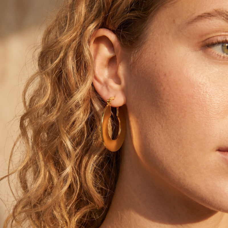 Side view of a model wearing a matte 18K gold PVD stainless steel Alandra hoop earring.