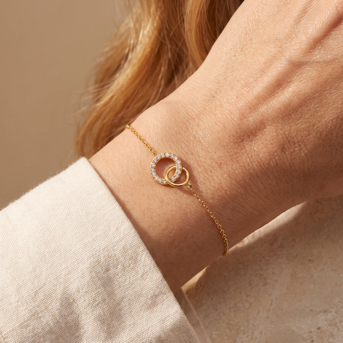Close-up of the gold-tone bracelet worn on a wrist, showing its interlocking polished and cubic zirconia-set circles.