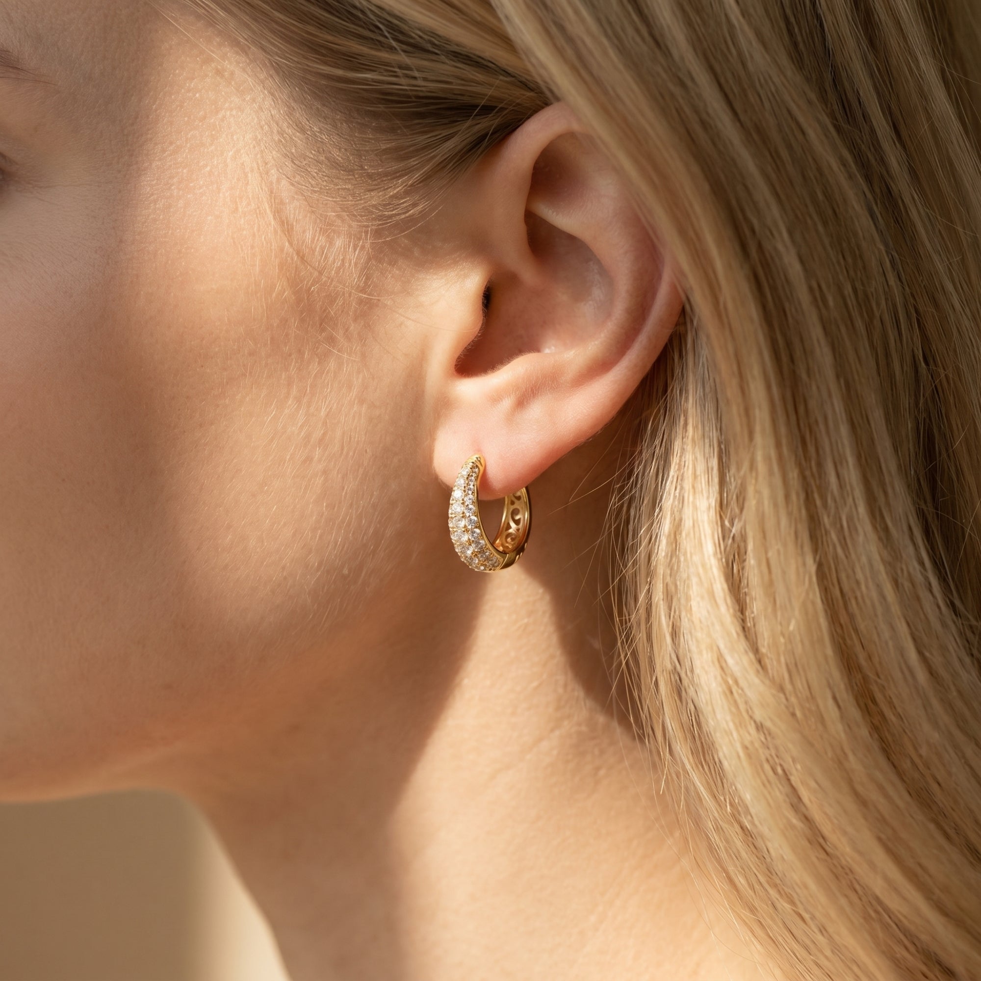 Gold moissanite hoop earrings with rows of round stones worn on a woman's ear.
