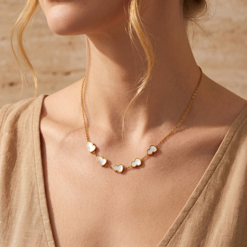 Gold station necklace with five white mother-of-pearl gourd motifs worn on a model in a beige top.