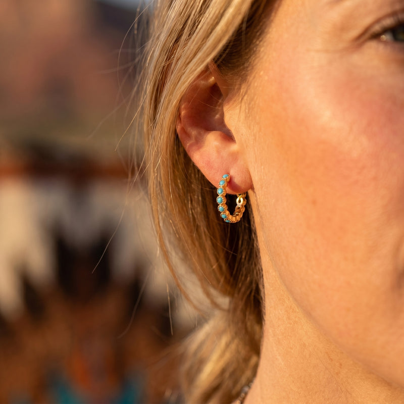 Close-up of a woman wearing a gold vermeil huggie earring set with round turquoise cabochons.